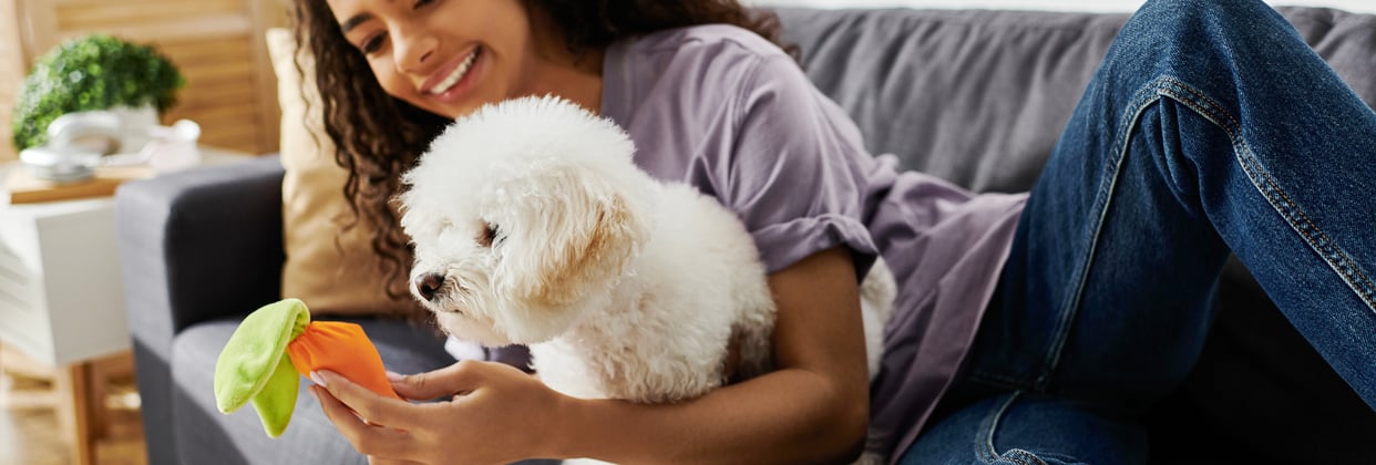 A woman sitting on a couch with her Bichon Frise dog.