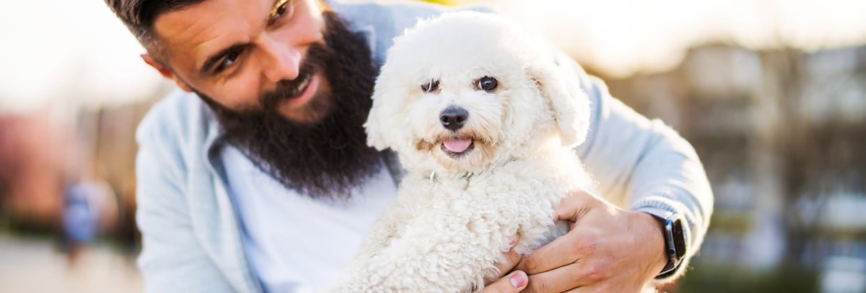 A man with a beard holding a Bichon Frise.