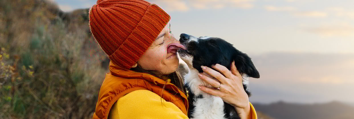 Owner wearing an orange beanie holding dog who is licking owner's face