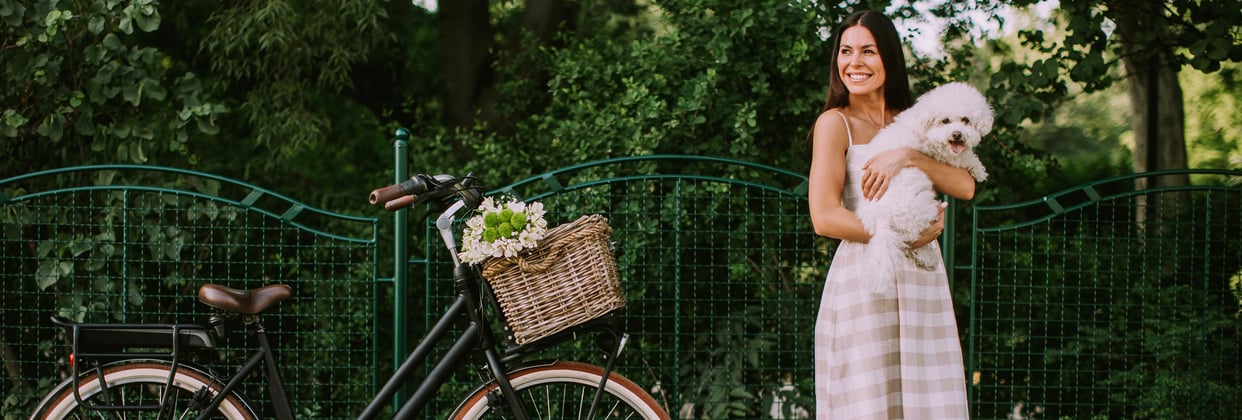 A woman standing next to a bicycle and holding a bichon frise