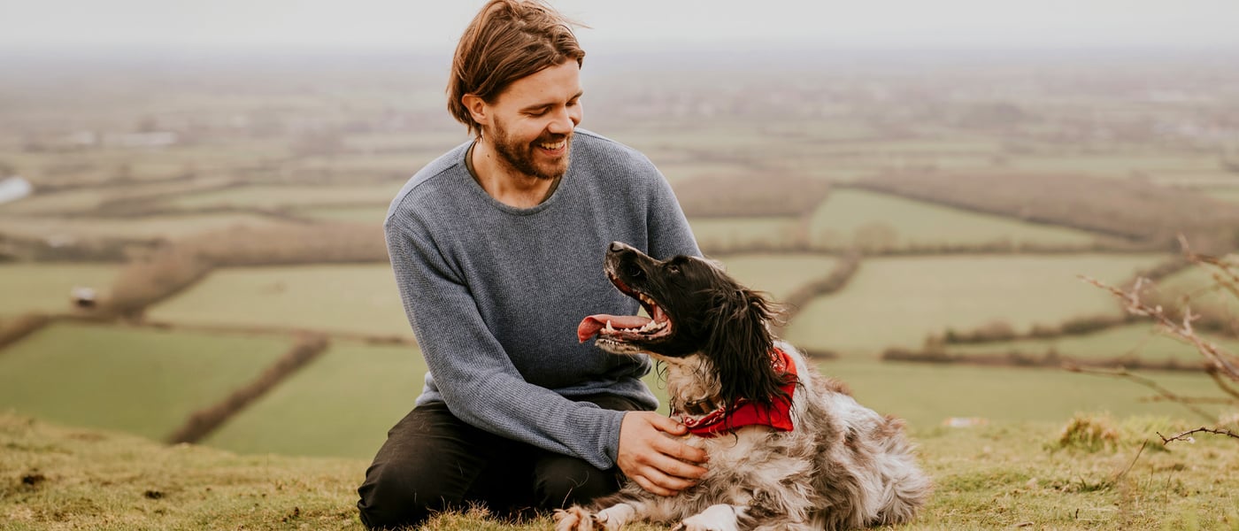 man with springer spaniel dog sitting above fields