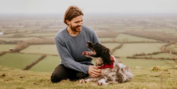 man with springer spaniel dog sitting above fields