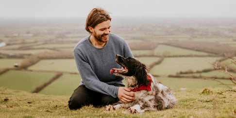 man with springer spaniel dog sitting above fields