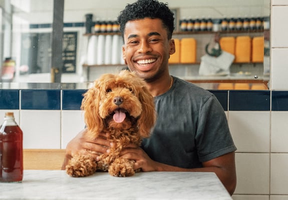 A man sits with his dog in a pie shop, they're both facing the camera with happy expressions.