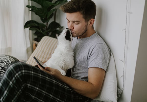 A person using a mobile phone while holding their cat in their lap. The cat is rubbing against their face.