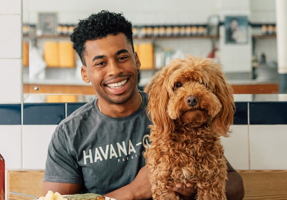 A man smiling in a cafe with his Cavapoo.