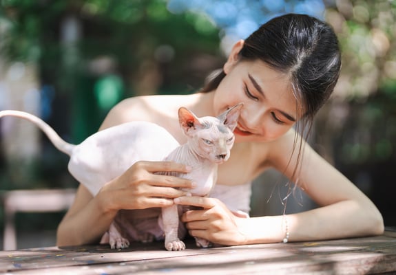 A girl and her sphynx cat outside at a table.