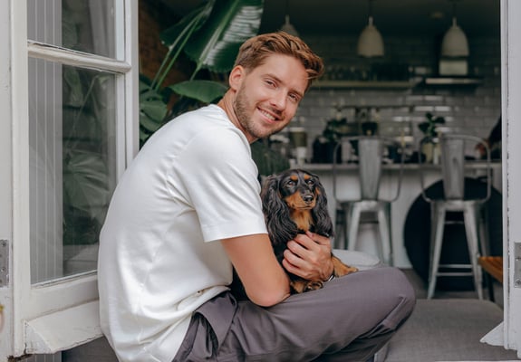 man sitting in the window of a kitchen with Dachshund sitting in his lap