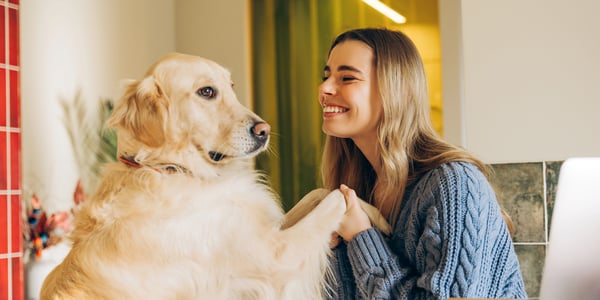 A smiling woman holding her dog's hand.