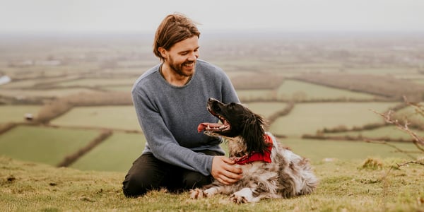 man with springer spaniel dog sitting above fields