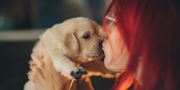 A woman with red hair kissing a puppy.