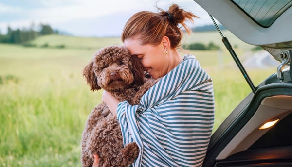 A woman in a striped blanket hugging her Maltipoo.