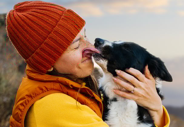 Owner wearing an orange beanie holding dog who is licking owner's face
