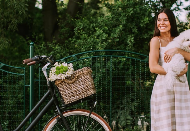 A woman standing next to a bicycle and holding a bichon frise