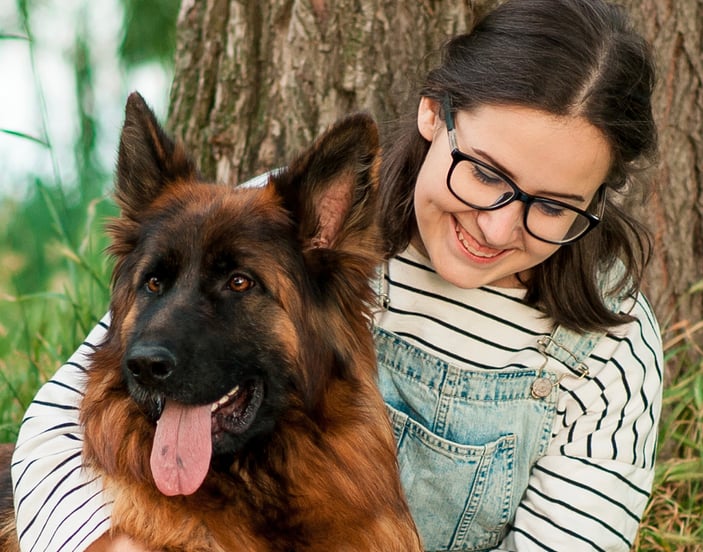 A girl reading a book against the tree with her German Shepherd in her arms