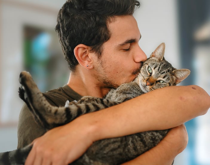 A man cuddling and kissing his tabby cat.