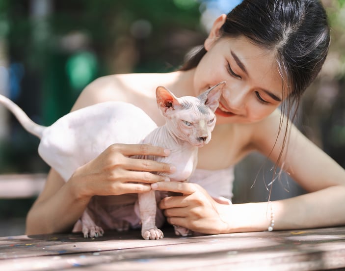 A girl and her sphynx cat outside at a table.
