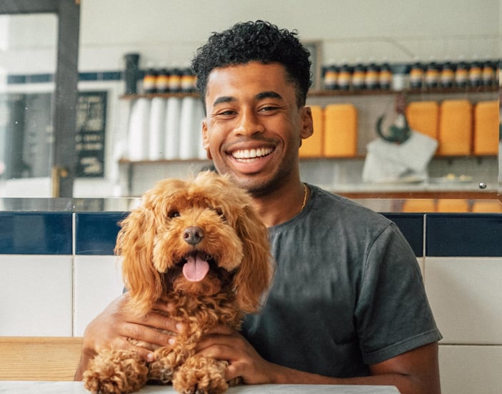 A man sits with his dog in a pie shop, they're both facing the camera with happy expressions.