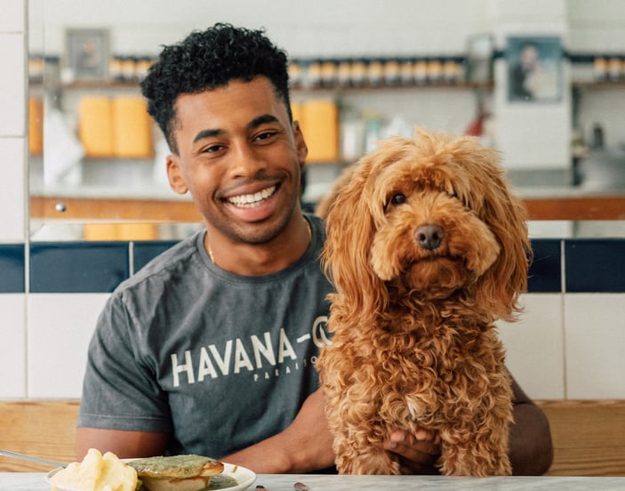A man smiling in a cafe with his Cavapoo.