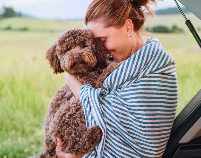 A woman in a striped blanket hugging her Maltipoo.