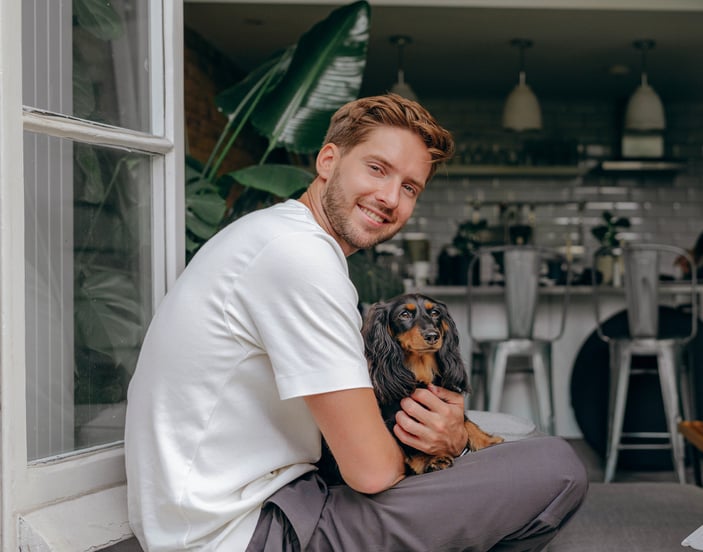 man sitting in the window of a kitchen with Dachshund sitting in his lap