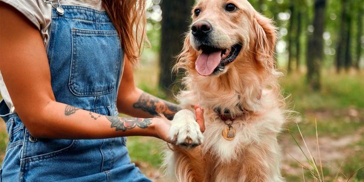 A tattooed woman in dunagrees holding her dog's hand.