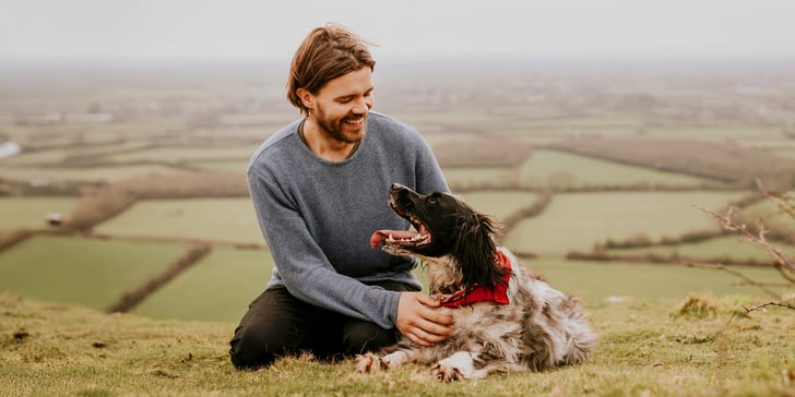 man with springer spaniel dog sitting above fields
