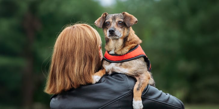 A woman holding a dog over her shoulder.