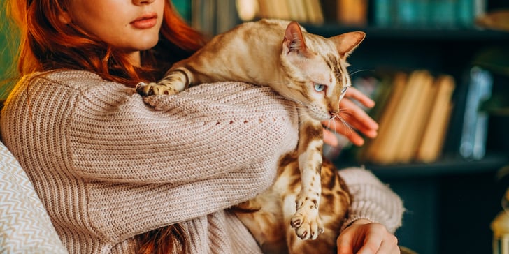 A woman holding a Bengal cat who's about to jump out of her hands.