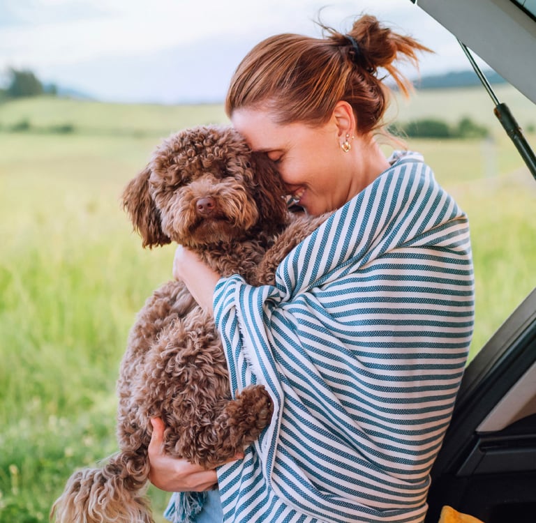 A woman in a striped blanket hugging her Maltipoo.