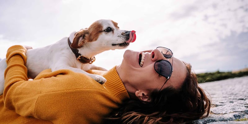 A happy woman with a white dog licking her face