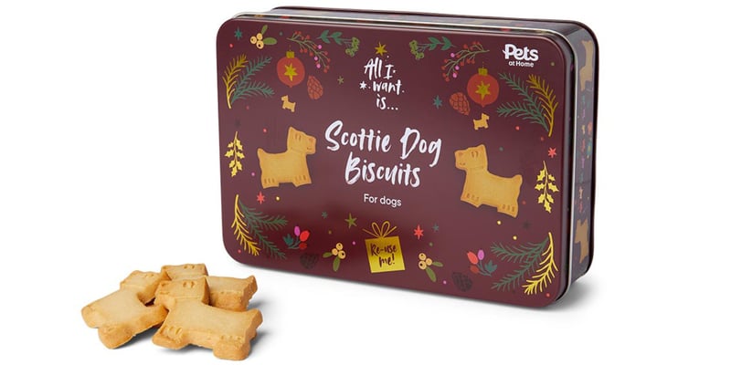 a scottie dog biscuit tin standing up with some treats laid out next to it