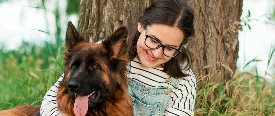 A girl reading a book against the tree with her German Shepherd in her arms