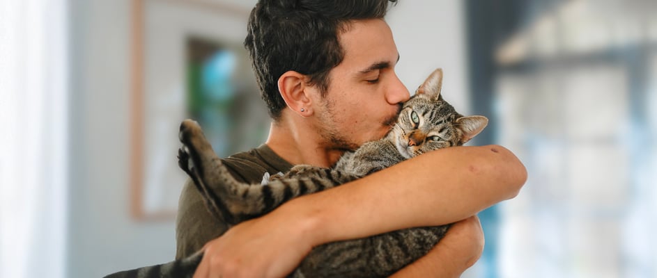 A man cuddling and kissing his tabby cat.