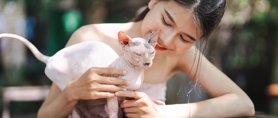 A girl and her sphynx cat outside at a table.