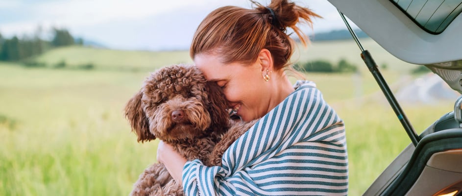A woman in a striped blanket hugging her Maltipoo.