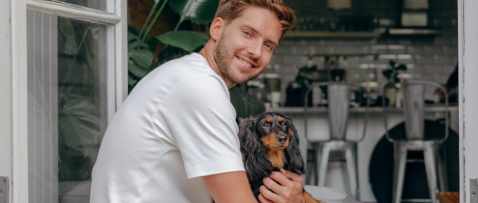 man sitting in the window of a kitchen with Dachshund sitting in his lap
